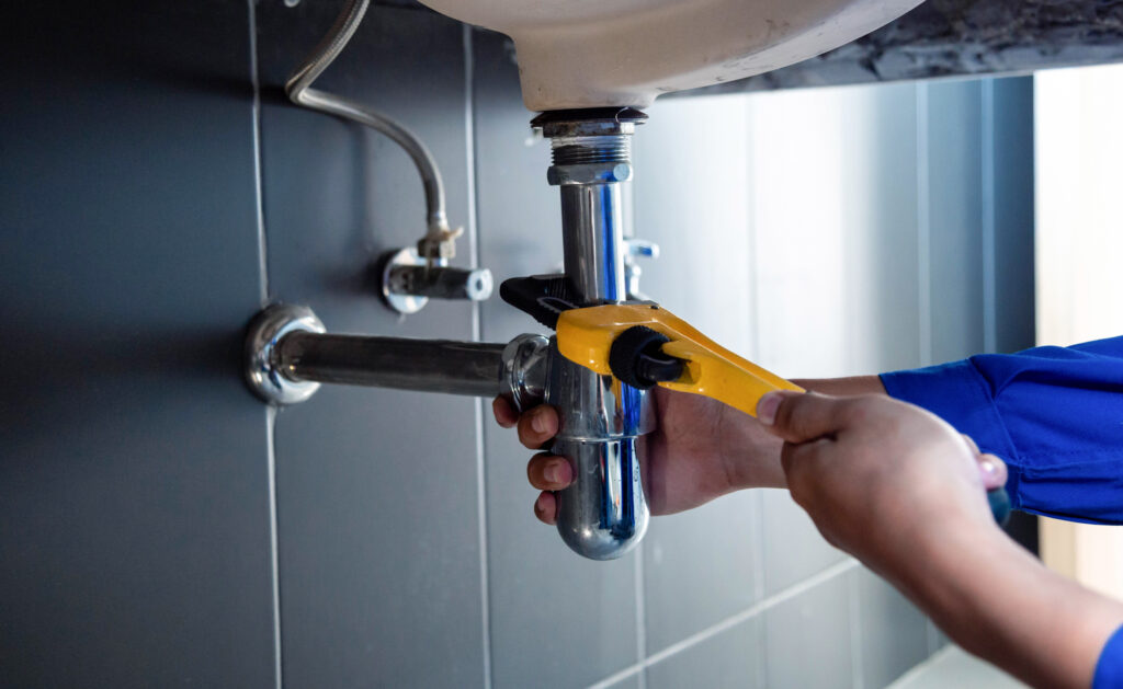 Plumber fixing white sink pipe with adjustable wrench